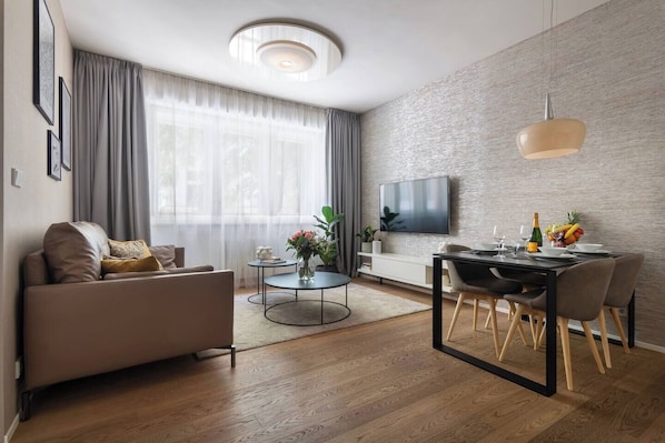 Ein modernes Wohnzimmer mit Sofa, Couchtisch, Esstisch und Fernseher.