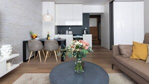Eine moderne Küche mit weißen Schränken, ein Essbereich mit einem runden Tisch und Stühlen sowie ein Wohnzimmer mit einer Couch und einem Couchtisch.