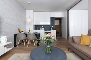 Eine moderne Küche mit weißen Schränken, ein Essbereich mit einem runden Tisch und Stühlen sowie ein Wohnzimmer mit einer Couch und einem Couchtisch.