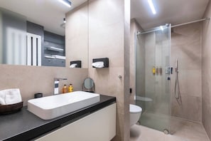 Ein modernes Badezimmer mit großem Waschbecken, Spiegel und Duschkabine aus Glas.