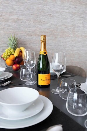 Ein Tisch, gedeckt mit einer Flasche Veuve Clicquot Champagner, leeren Weingläsern, weißen Tellern und einer Obstschale.