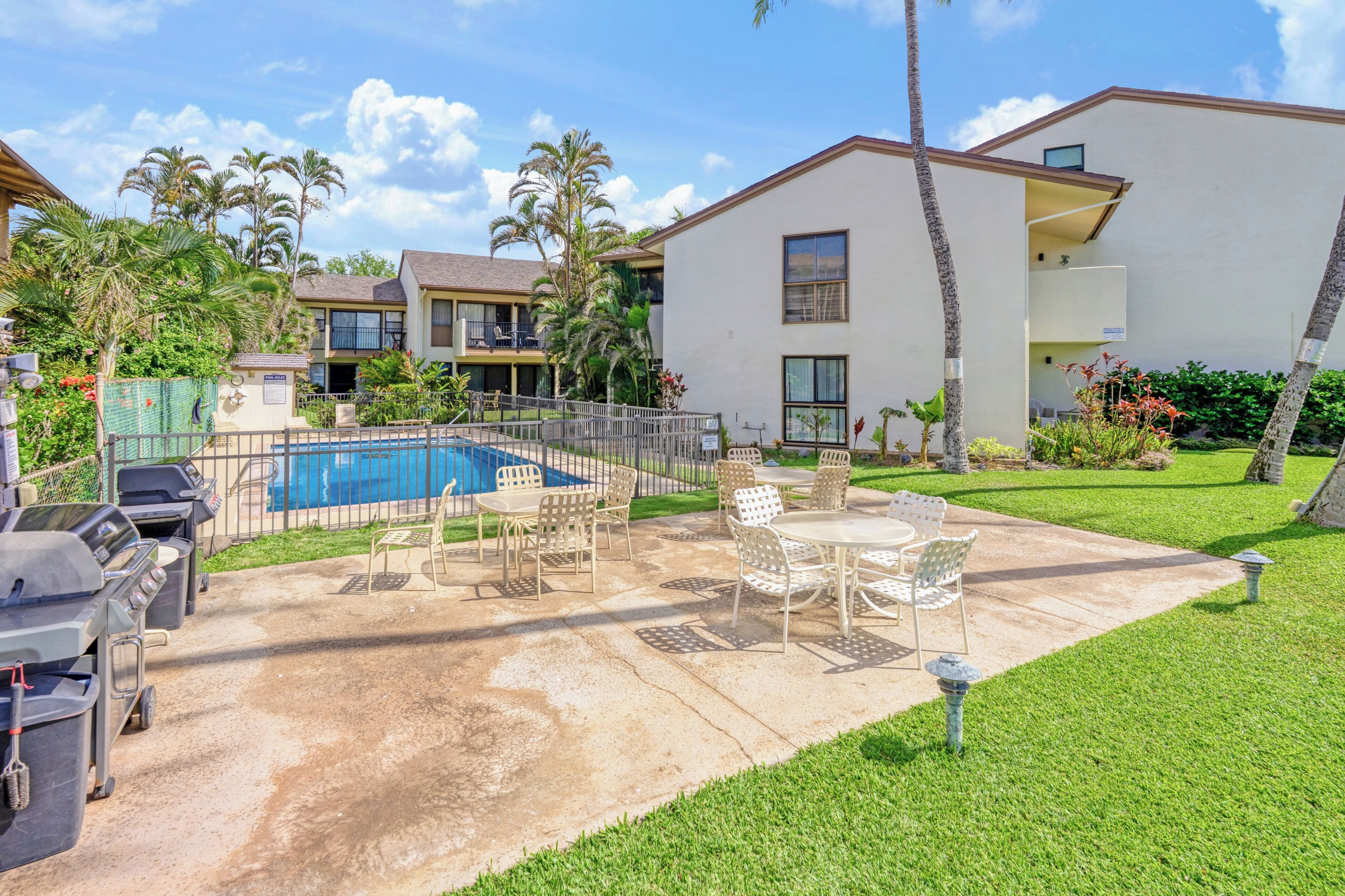 A residential building with a swimming pool, outdoor patio with chairs, and a barbecue grill.