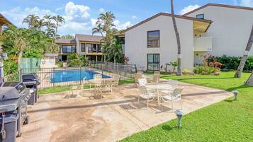A residential building with a swimming pool, outdoor patio with chairs, and a barbecue grill.