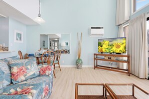 Una sala de estar con sofá, televisor, mesa de comedor con sillas, un jarrón y un espejo.