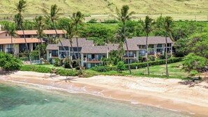 A beachfront hotel with multiple-story buildings, a sandy beach, and palm trees. - Ocean-view 2BR Maui condo with pool, A/C, beach (Wailuku)