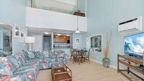 A living room with a sectional sofa, dining table, chairs, and a television. - Ocean-view 2BR Maui condo with pool, A/C, beach (Wailuku)