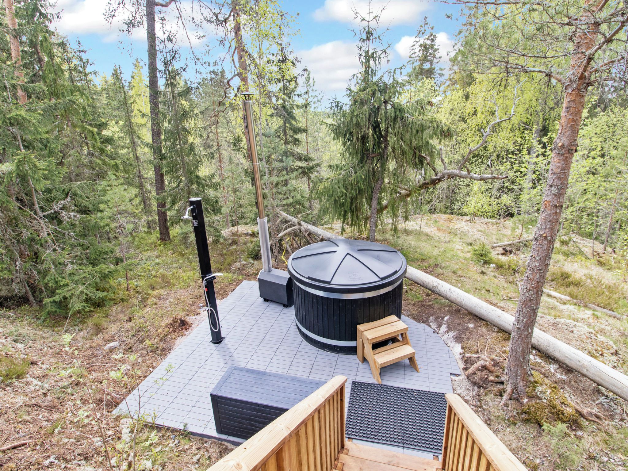 A hot tub surrounded by a wooden deck, a wooden bench, and a metal grate.