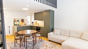A modern living room with a sofa, a dining table with chairs, a kitchen area, and a staircase.