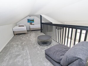 Un dormitorio loft pequeño y moderno con dos camas, una mesa redonda y barandilla de balcón.