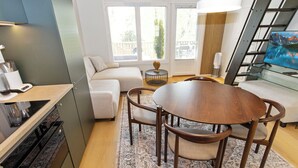 A modern kitchen with a dining area, a sofa, and a staircase with a TV.