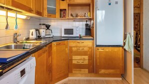 Eine kleine Küche mit Holzausstattung, einem Geschirrspüler von Bosch, einer Mikrowelle und einem Kühlschrank.