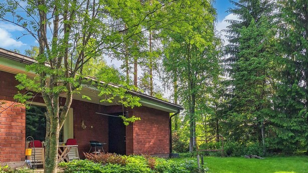Ein Backsteinhaus mit überdachter Veranda, umgeben von üppigem Grün und Bäumen.