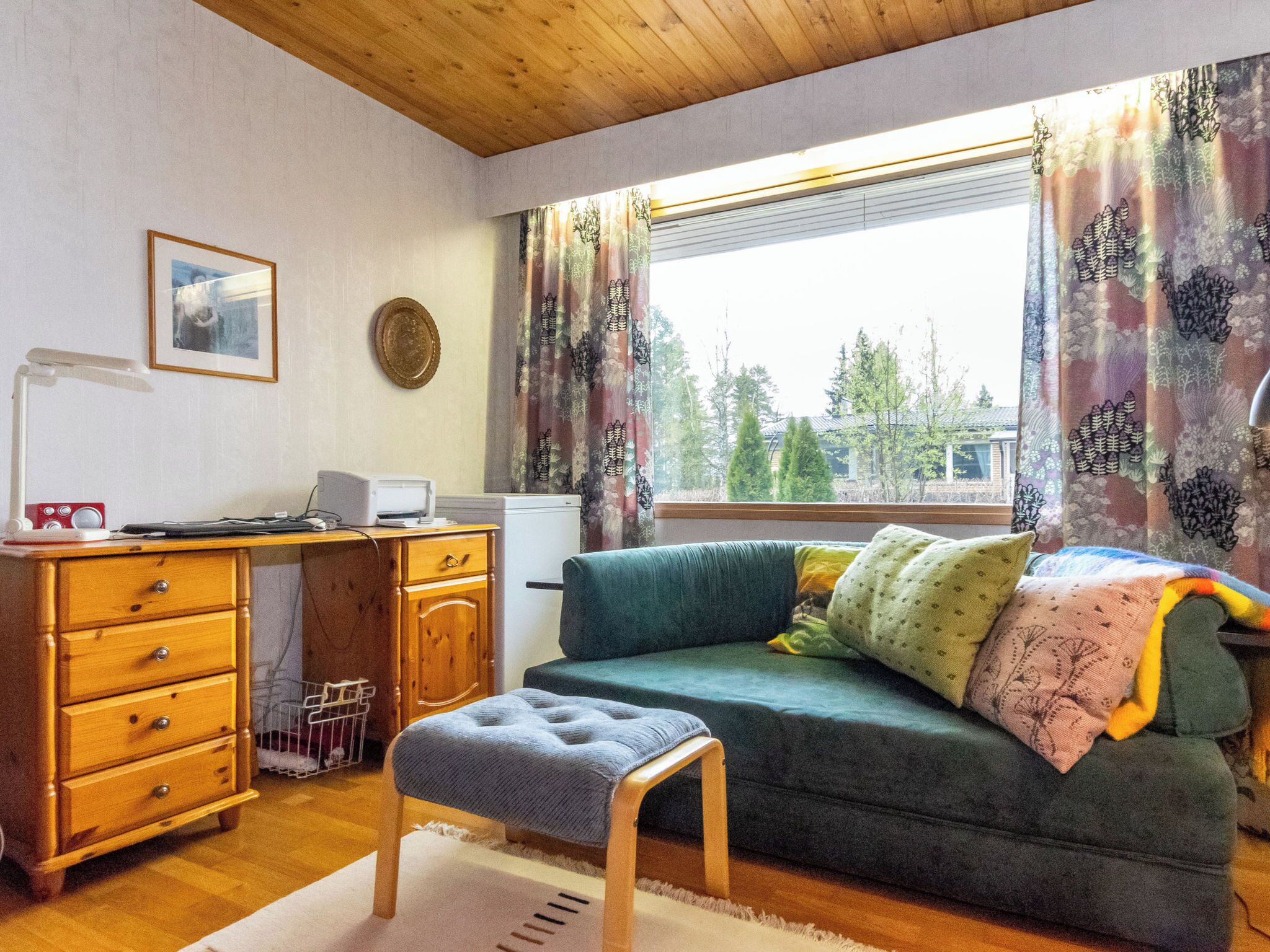 Een kamer met een houten bureau, een computer, een printer, een bank en een raam met gordijnen.