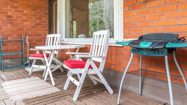 Une terrasse extérieure avec un mur en briques, une table avec des chaises et un barbecue.