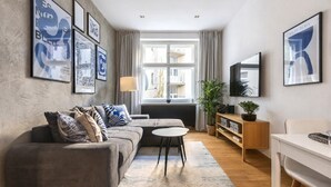 A modern living room with a grey sofa, a small round table, a TV, and framed artwork on the walls. - Stylish Apartment in Prague's Historic Centre (Prague 1)