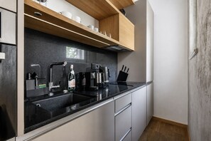 A modern kitchen with a black countertop, stainless steel appliances, and wooden shelves above the sink. - Stylish Apartment in Prague's Historic Centre (Prague 1)