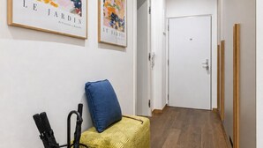 A hallway with wooden flooring, a yellow patterned sofa with a blue cushion, and two framed artworks on the wall. - Stylish Apartment in Prague's Historic Centre (Prague 1)