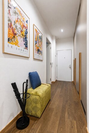 A hallway with wooden flooring, a yellow patterned sofa with a blue cushion, and two framed artworks on the wall. - Stylish Apartment in Prague's Historic Centre (Prague 1)