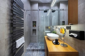 A modern bathroom with a glass shower enclosure, a wooden vanity with a sink, and a towel rack. - Stylish Apartment in Prague's Historic Centre (Prague 1)