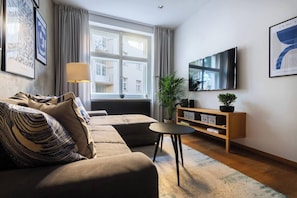 A modern living room with a sofa, a small table, a TV, and a window with curtains. - Stylish Apartment in Prague's Historic Centre (Prague 1)
