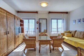 Ein Wohnzimmer mit Korbmöbeln, einem gelben Sofa und einem Tisch mit Glasplatte.