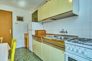 Eine kompakte Küche mit Gaskochfeld, zwei Spülen, einem Kühlschrank, Holzschränken und einem kleinen Holztisch.