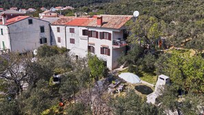 A white building with red shutters and a satellite dish, surrounded by trees and hills. - Apartment 2440/244326 (Kvarner - Martinšćica), 200m from the beach (Martinšćica)