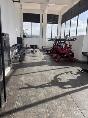 Ein Fitnessraum mit Trainingsgeräten, großen Fenstern und einem gefliesten Boden.