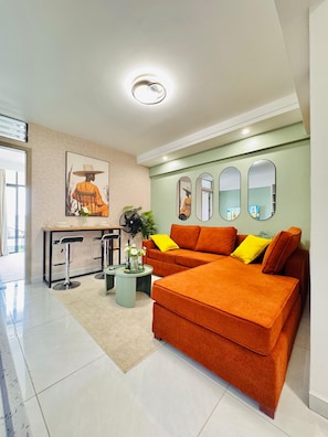 Ein modernes Wohnzimmer mit einer Couch, einem Esstisch und zwei Stühlen. An der Wand befinden sich drei Spiegel und ein Gemälde über der Couch.