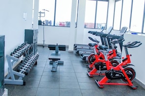 Ein Fitnessraum mit Trainingsgeräten, darunter Hanteln, Bänke und Fahrrädern.