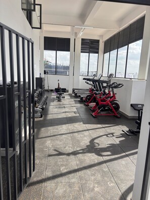 A gym with exercise equipment, a water bottle, and a window with a view. - Cozy 1-bedroom apartment in Nairobi, Westlands at the heart of the city (nairobi)