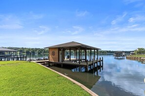 Une structure de type belvédère, dotée d’un toit et de murs, située sur une jetée qui s’avance sur un lac paisible.