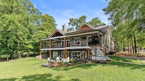 A two-story house with a porch, a stone foundation, and a well-maintained lawn. - Lake Sinclair Paradise|Beach|Game Rm|Dog-Friendly (Eatonton)