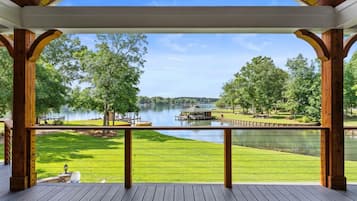 Une terrasse couverte avec vue sur un lac, une terrasse en bois et une zone herbeuse.