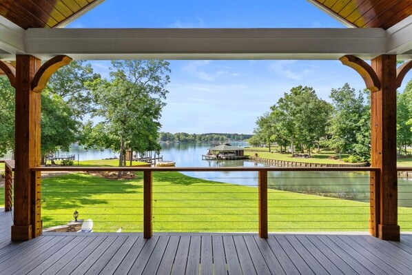 A covered deck with a view of a lake, wooden deck, and a grassy area.