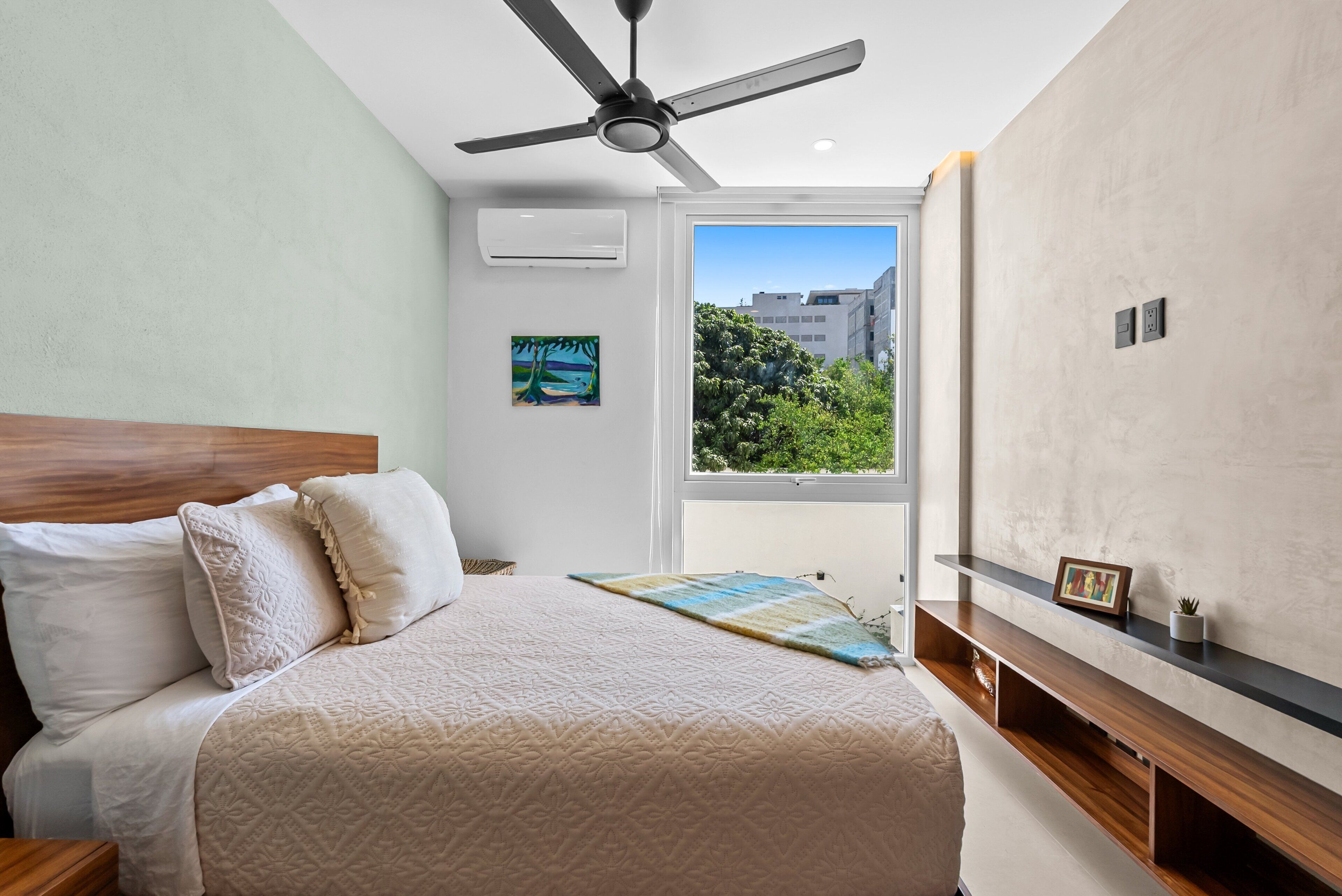 Une chambre comprenant un lit, un ventilateur de plafond, un appareil de climatisation, des œuvres d’art, une fenêtre et des étagères intégrées.