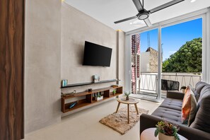 Ein modernes Wohnzimmer mit Flachbildfernseher, Holzregalen, einer Couch und Blick auf ein Gebäude und Bäume.