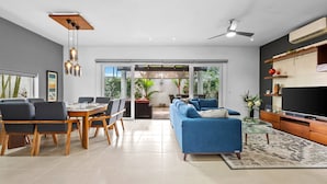 Ein modernes Wohnzimmer mit Essbereich, einem blauen Sofa, einem Fernseher und einem Deckenventilator.