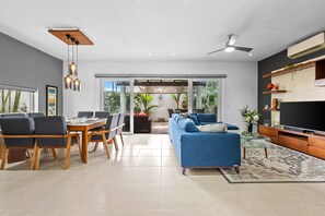 A modern living room with a dining area, a blue sofa, a TV, and a ceiling fan. - 4BR Family Villa with Pool, Gym & Private Parking (Nuevo Vallarta)