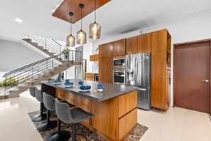 A modern kitchen with a central island, stainless steel appliances, and a wooden cabinet. - 4BR Family Villa with Pool, Gym & Private Parking (Nuevo Vallarta)