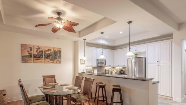 Una cocina moderna con armarios blancos, una isla central, iluminación colgante y un ventilador de techo.