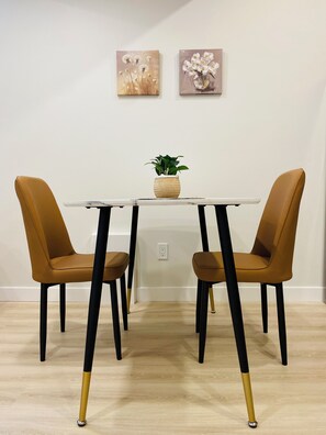 A dining table with two chairs, a potted plant, and two wall-mounted paintings. - *BRAND NEW*Downtown*Rogers Place*Cozy Guest Suite (Edmonton)