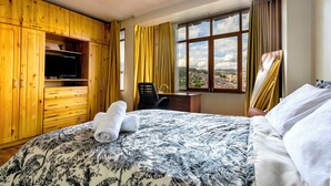 A hotel room with a bed, a desk, a chair, a television, and a window with curtains. - 5 min to the center! | Beautiful and homely | Incredible views & private parking (Cusco)