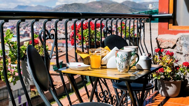 A balcony with a table set for breakfast, including a glass of orange juice, a plate, a mug, and a teapot. - 5 min to the center! | Beautiful and homely | Incredible views & private parking (Cusco)