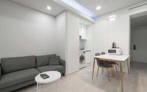 A modern living space with a grey sofa, a small round table, a dining table with chairs, a washing machine, and a microwave. - BS centum hotel (Busan)