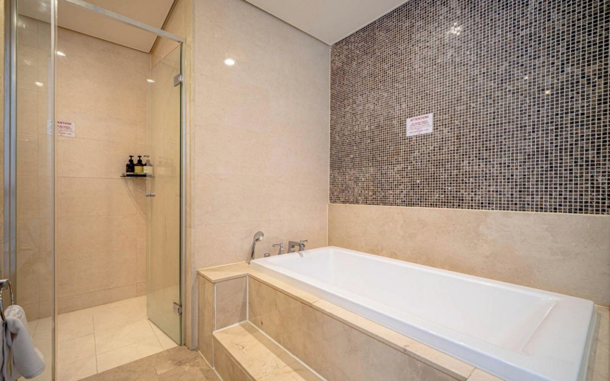 A modern bathroom with a glass shower enclosure, a freestanding bathtub, and a mosaic tile wall.