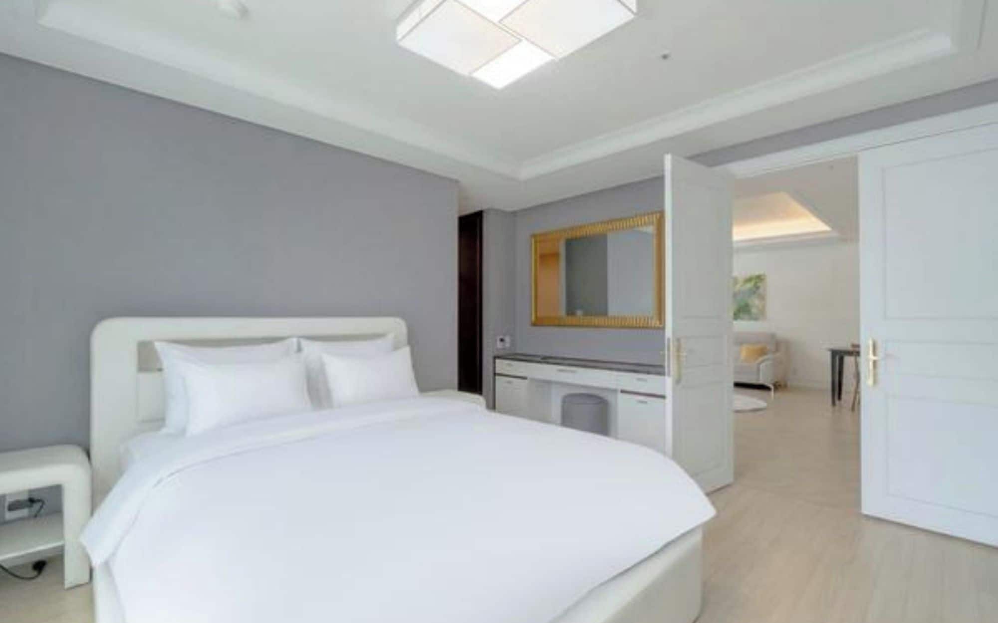 A modern bedroom with a large bed, a bedside table, a mirror, and a wardrobe.