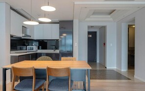 A modern kitchen with built-in appliances, a dining table with chairs, and a visible hallway leading to another room.