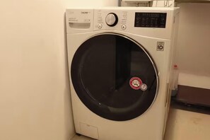 A front view of a white washing machine with a control panel, a circular door, and a red sticker on the door. - BS centum hotel (Busan)
