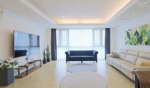 Ein modernes Wohnzimmer mit Flachbildfernseher, zwei Sofas, einem Couchtisch und einem großen Fenster mit transparenten Vorhängen.
